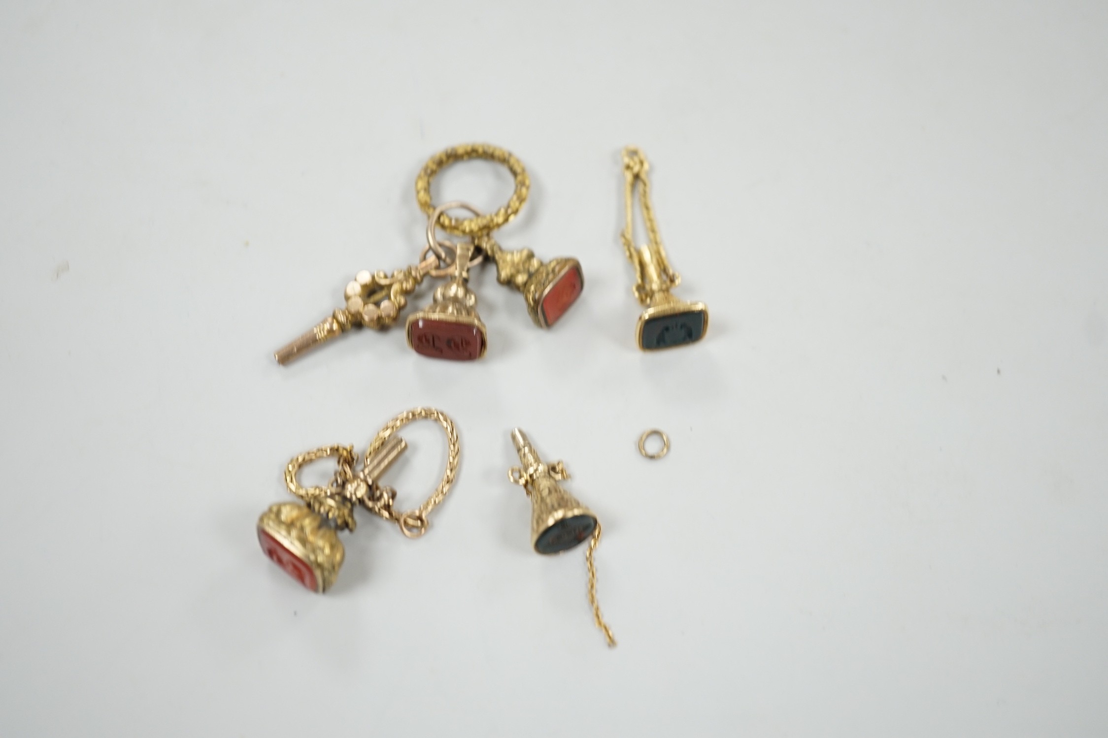 Two 19th century yellow metal overlaid and bloodstone set watch key fobs, one of funnel form, 21mm, a similar gold plated and carnelian set watch key fob, two other fob seals and a watch key on chain.
